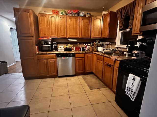 kitchen with appliances with stainless steel finishes, sink, dark stone counters, and light tile patterned floors