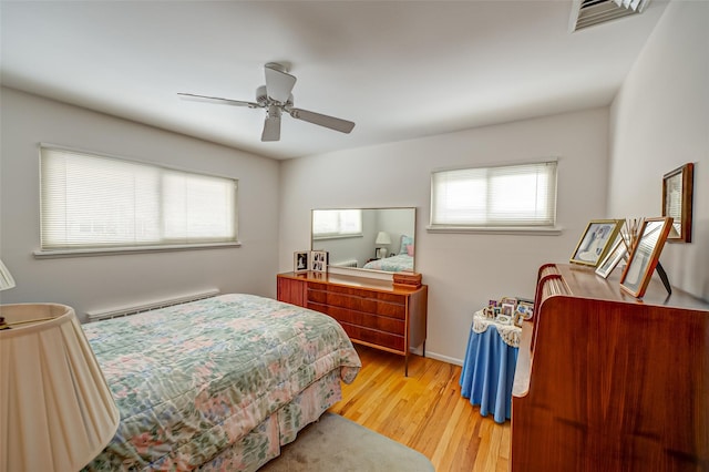 bedroom with a baseboard heating unit, wood finished floors, visible vents, baseboards, and a ceiling fan