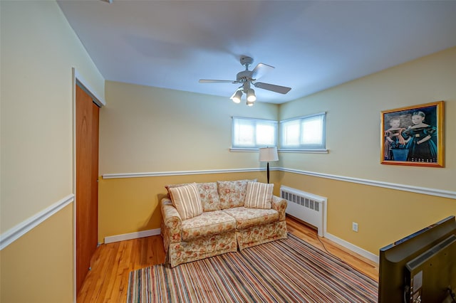 living area with baseboards, ceiling fan, radiator heating unit, and light wood-style floors