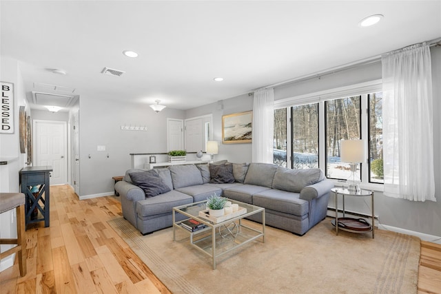 living room with attic access, a baseboard radiator, visible vents, and light wood finished floors