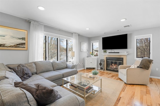 living area with light wood-style flooring, plenty of natural light, a fireplace with flush hearth, and visible vents