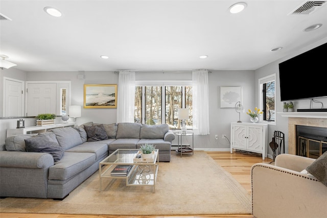 living area with recessed lighting, visible vents, baseboards, light wood-type flooring, and a tiled fireplace