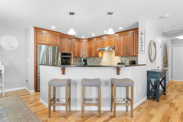 kitchen featuring brown cabinetry, dark stone counters, appliances with stainless steel finishes, a kitchen breakfast bar, and hanging light fixtures