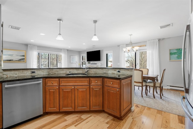 kitchen featuring visible vents, brown cabinetry, appliances with stainless steel finishes, dark stone countertops, and a sink