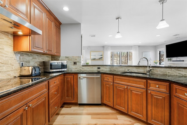 kitchen with stainless steel appliances, a sink, exhaust hood, dark stone counters, and pendant lighting