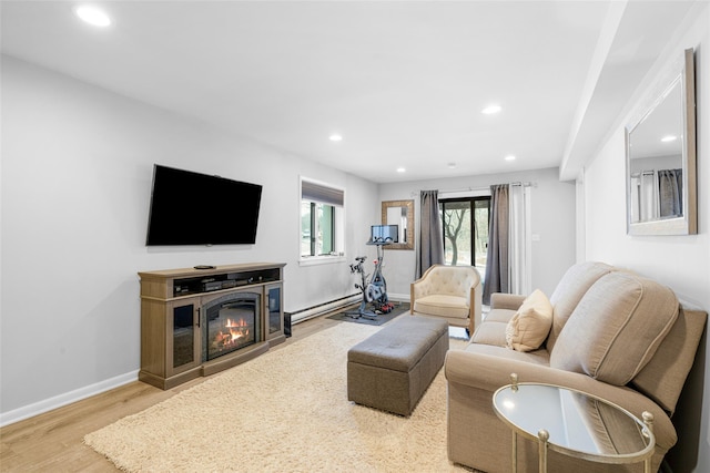 living area featuring a baseboard radiator, recessed lighting, baseboards, light wood finished floors, and a glass covered fireplace