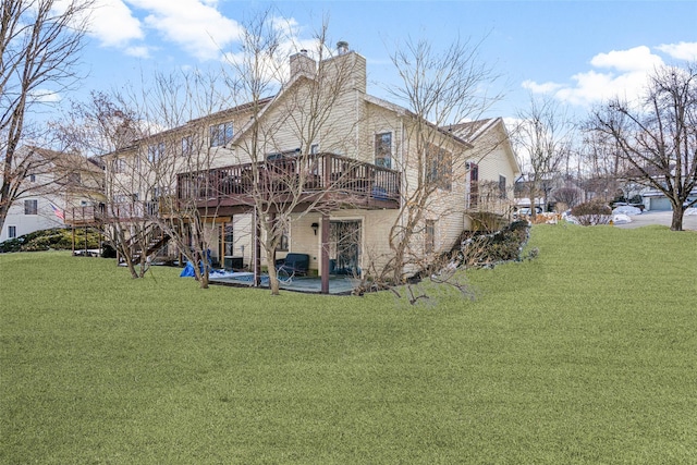 rear view of property with a deck, a patio area, a lawn, and a chimney