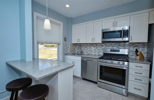 kitchen with a breakfast bar, a sink, appliances with stainless steel finishes, a peninsula, and white cabinets