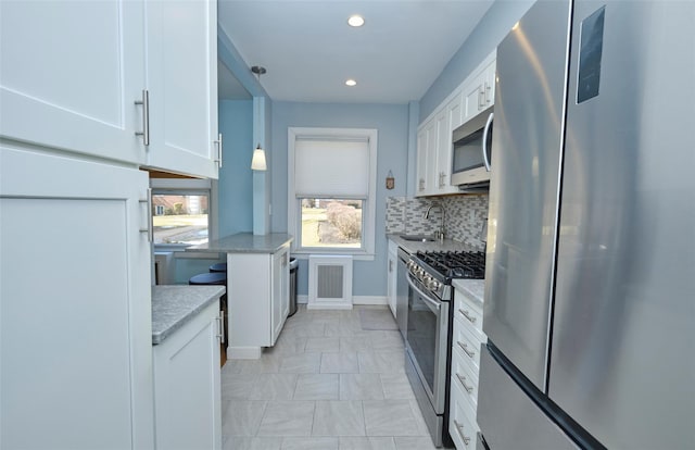 kitchen with a sink, light stone counters, appliances with stainless steel finishes, pendant lighting, and white cabinetry