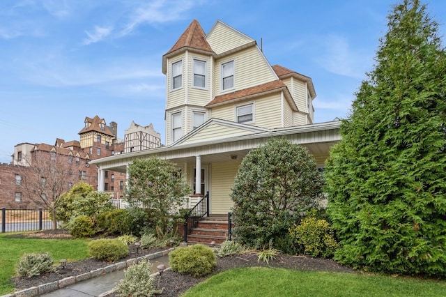 victorian-style house featuring covered porch, a front yard, and fence