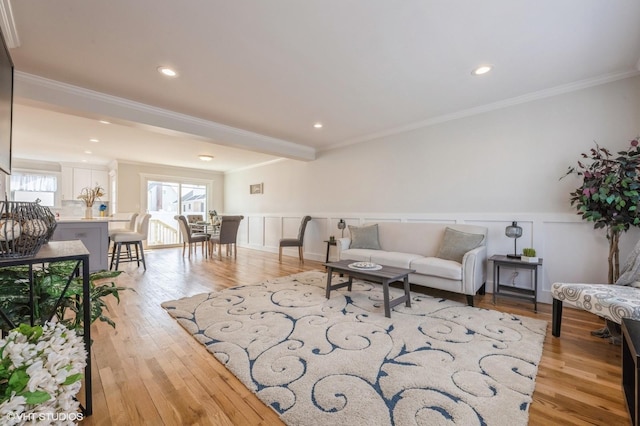 living room featuring light wood-type flooring, a wainscoted wall, ornamental molding, and a decorative wall