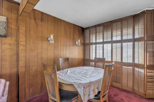 dining room featuring dark colored carpet and wood walls