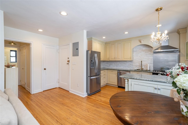 kitchen featuring hanging light fixtures, appliances with stainless steel finishes, wall chimney exhaust hood, and cream cabinetry