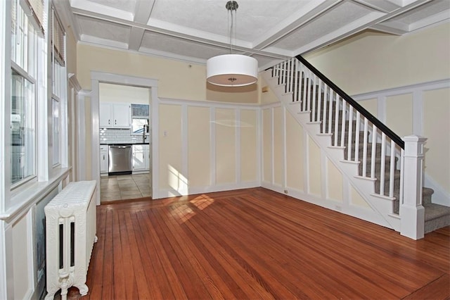 entryway featuring a decorative wall, coffered ceiling, stairs, radiator, and wood-type flooring