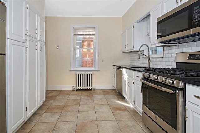 kitchen with appliances with stainless steel finishes, white cabinets, and radiator heating unit