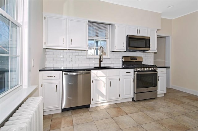 kitchen featuring radiator, dark countertops, stainless steel appliances, and a sink