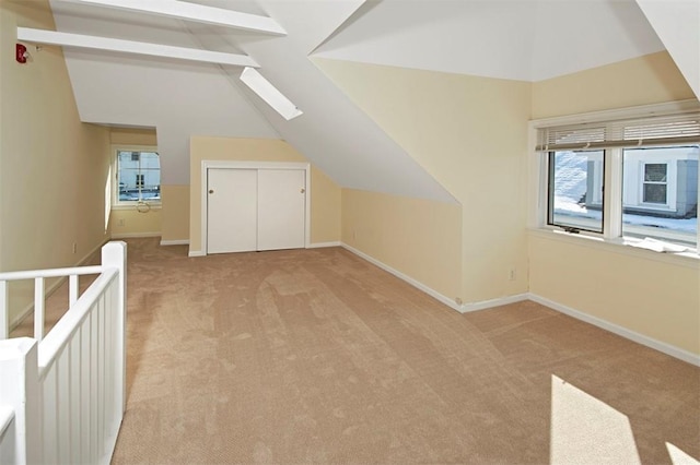 bonus room with a wealth of natural light, vaulted ceiling with skylight, light carpet, and baseboards