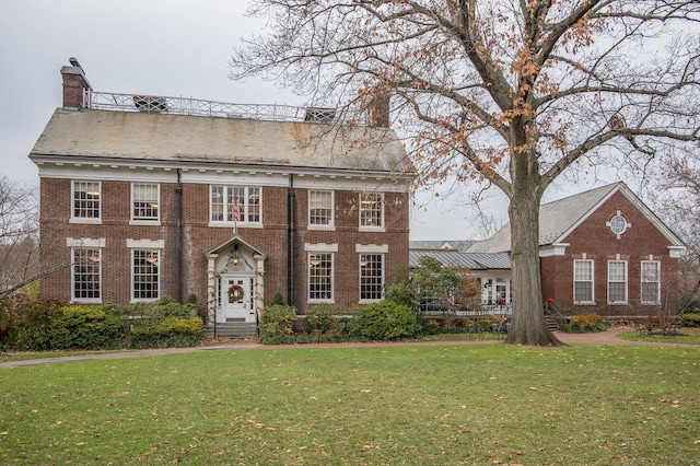 colonial-style house featuring brick siding, a chimney, and a front yard