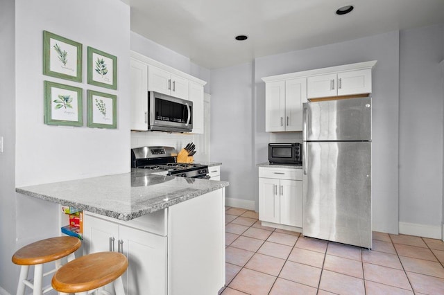 kitchen featuring appliances with stainless steel finishes, light tile patterned flooring, light stone counters, and white cabinets