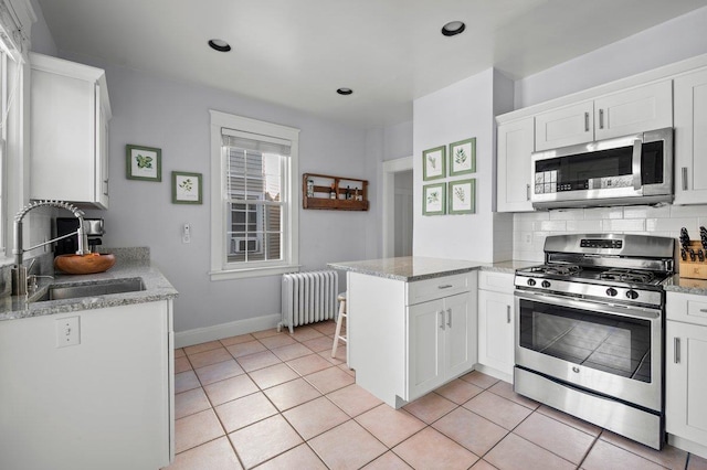 kitchen with tasteful backsplash, radiator heating unit, stainless steel appliances, white cabinetry, and a sink