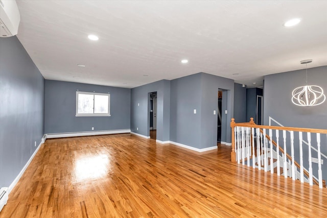 unfurnished room with a chandelier, a baseboard radiator, baseboards, and wood finished floors