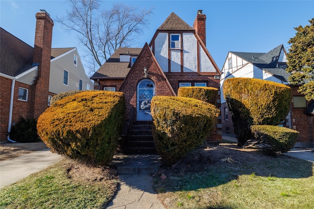 english style home featuring roof with shingles, a chimney, and brick siding