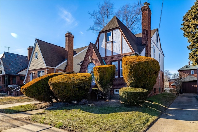 english style home featuring brick siding, a chimney, and a front lawn