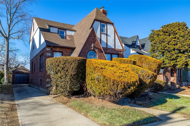 tudor home featuring driveway, a garage, a shingled roof, an outbuilding, and brick siding