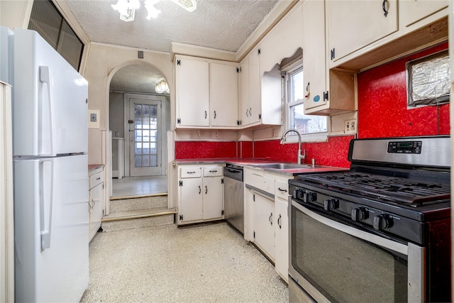 kitchen with arched walkways, appliances with stainless steel finishes, white cabinetry, a sink, and a textured ceiling