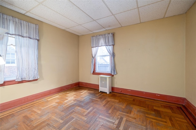 unfurnished room featuring radiator, a drop ceiling, and baseboards