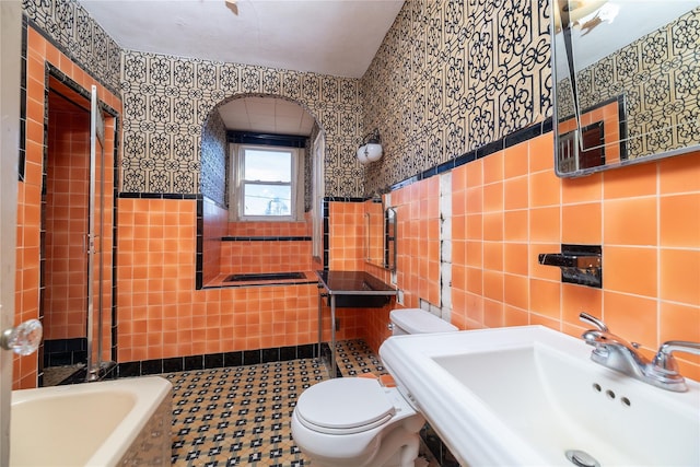 full bath with a sink, tile walls, toilet, and a bath