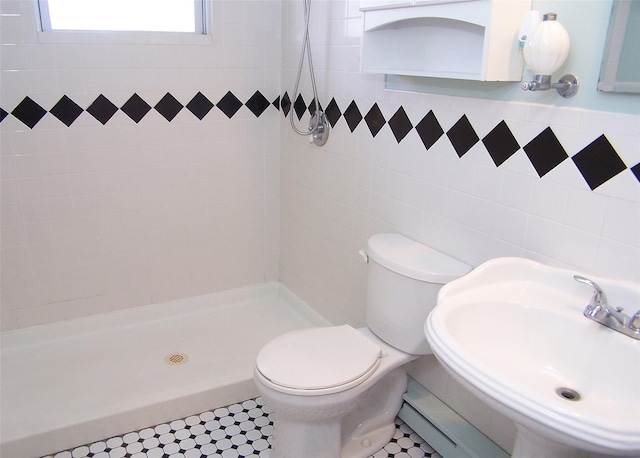 full bath featuring tiled shower, a sink, toilet, and tile walls