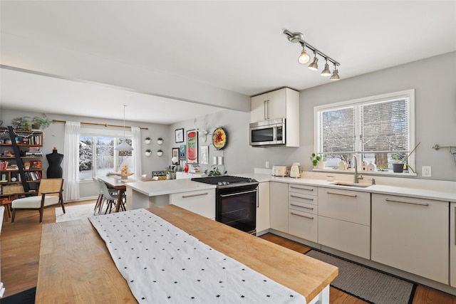 kitchen with light hardwood / wood-style flooring, sink, gas stove, pendant lighting, and kitchen peninsula