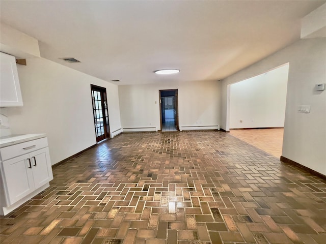 unfurnished living room featuring brick floor, a baseboard heating unit, baseboards, and visible vents