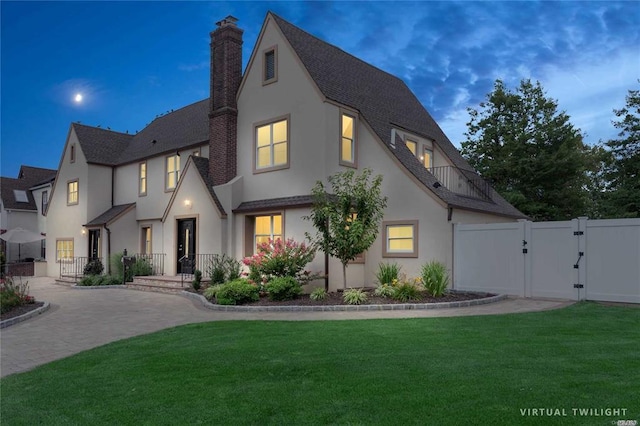 view of front of home featuring a chimney, a gate, fence, a yard, and stucco siding