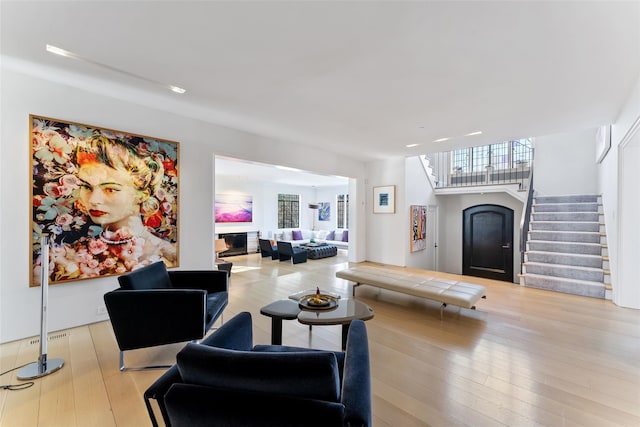 living area with stairway, a glass covered fireplace, and light wood-style floors