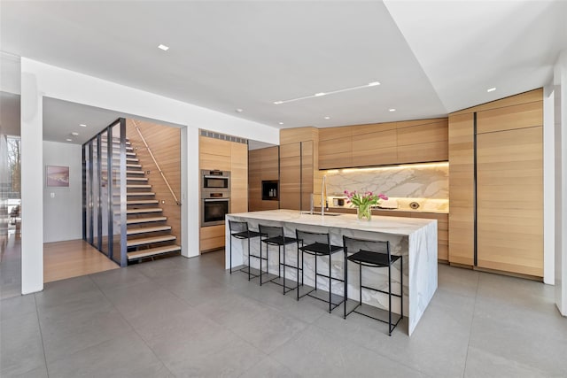 kitchen with a kitchen island with sink, a sink, a kitchen breakfast bar, light countertops, and modern cabinets