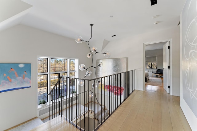 hallway with light wood-style floors, lofted ceiling, a chandelier, and an upstairs landing