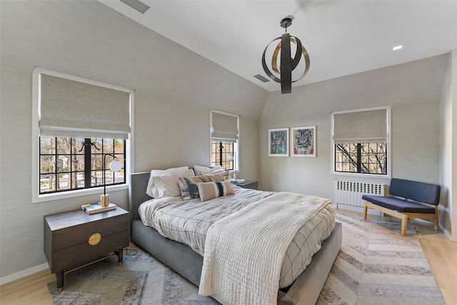 bedroom featuring visible vents, baseboards, light wood-style floors, vaulted ceiling, and radiator