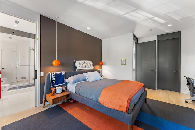 bedroom with ensuite bathroom, light wood finished floors, and visible vents