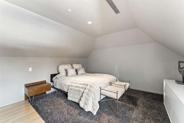 bedroom with lofted ceiling, wood finished floors, visible vents, and baseboards