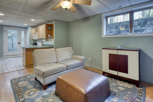 living area with ceiling fan, light wood finished floors, baseboards, and a paneled ceiling