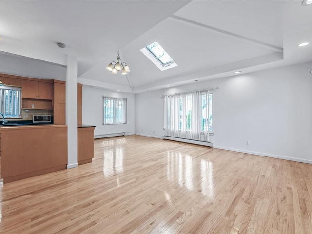 unfurnished living room with vaulted ceiling with skylight, a raised ceiling, baseboard heating, light wood-type flooring, and a baseboard heating unit