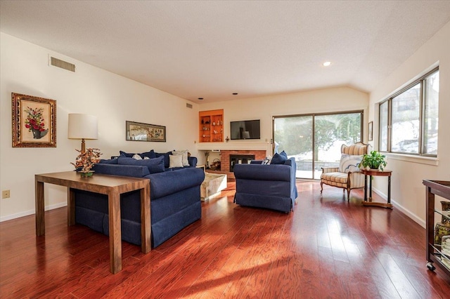 living area featuring a brick fireplace, dark wood finished floors, visible vents, and baseboards