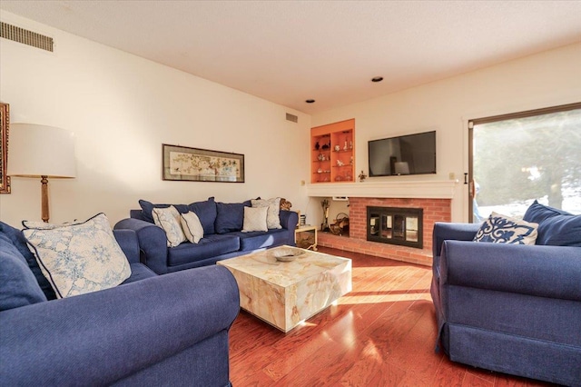 living room featuring built in shelves, a brick fireplace, wood finished floors, and visible vents