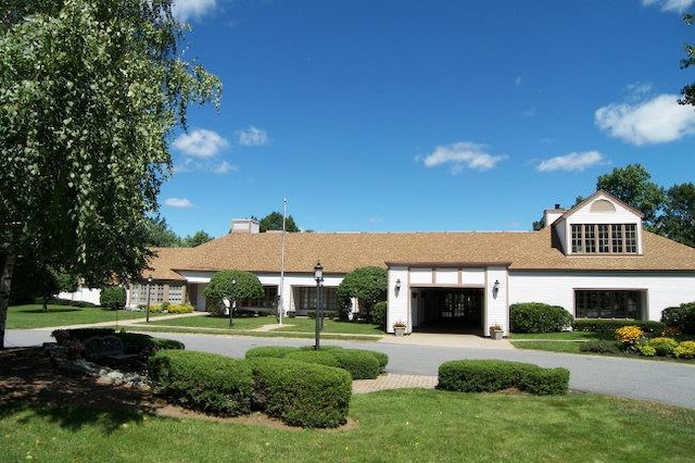 view of front of home featuring a garage, a chimney, curved driveway, and a front lawn