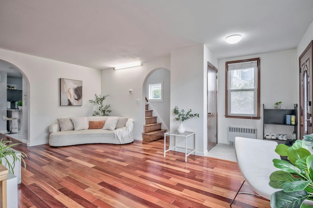 living room with light wood-style flooring, arched walkways, radiator, and stairway