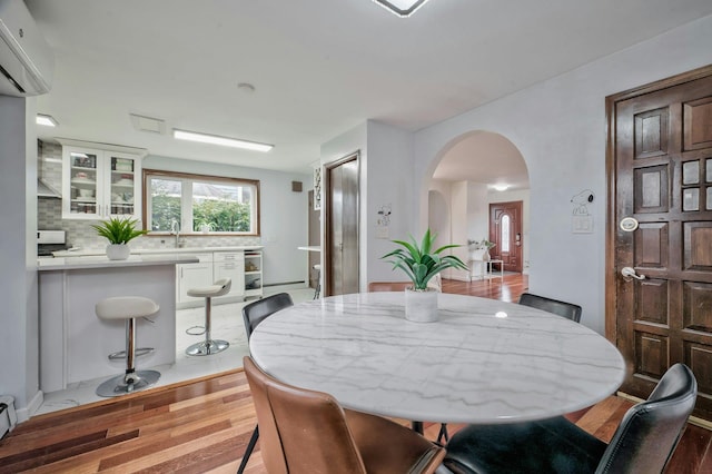 dining space with a wall unit AC, arched walkways, and wood finished floors