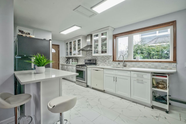 kitchen with wall chimney exhaust hood, appliances with stainless steel finishes, marble finish floor, light countertops, and a sink