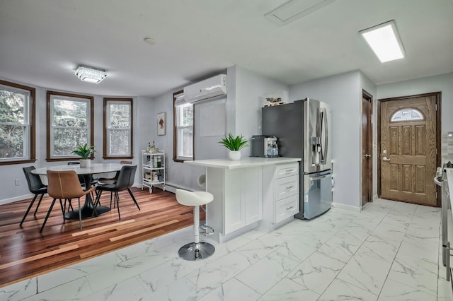 kitchen featuring marble finish floor, a wall unit AC, light countertops, stainless steel fridge, and baseboards